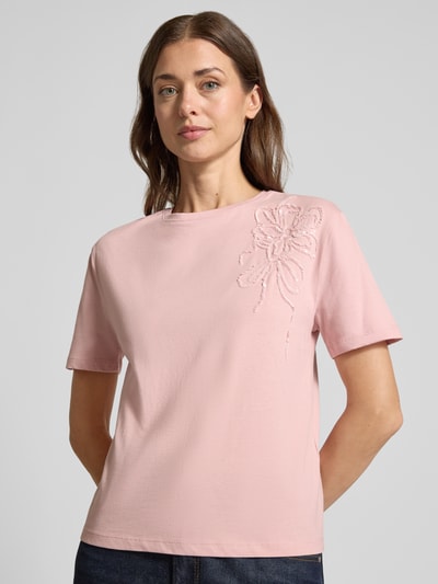 Frauenmodel trägt Regular Fit T-Shirt aus reiner Baumwolle mit Blumen-Applikation von Christian Berg Woman in Rosa, Nahaufnahme Oberkörper. Reine Baumwolle, Rundhalsausschnitt, kurzärmliges Design, überschnittene Schultern, Pailletten-Blumen, Rückenlänge bei Größe S 54 cm.