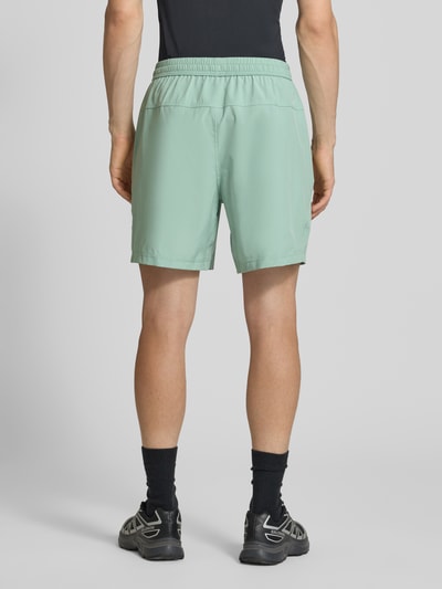 Mannenmodel draagt Shorts mit Logo-Print und Eingrifftaschen van NIKE TRAINING in mintgroen, recht model, binnenbeenlengte maat M 19 cm, bandwijdte maat M 41 cm, steekzakken, logoprint, elastische band met tunnelkoord. Ganzkörperaanzicht achterkant.