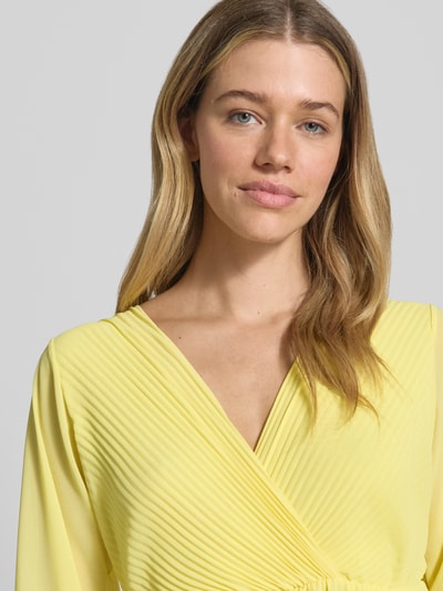 Frauenmodel trägt knielanges Kleid mit Plisseefalten Modell 'Im44sa' von ZABAIONE in Gelb, Wickel-Optik, Nahaufnahme Oberkörper.