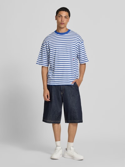 Männermodel trägt Oversized T-Shirt mit Label-Stitching von REVIEW in blau-weißem Allover-Look, Reine Baumwolle, Rundhalsausschnitt, Ganzkörperansicht von vorne.