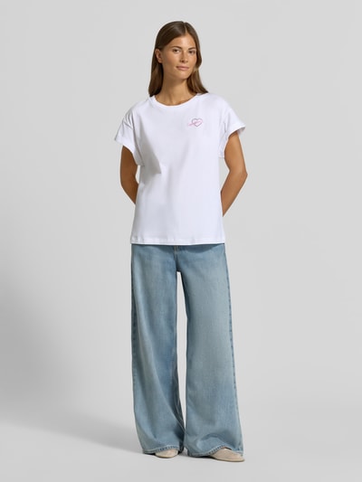 Frauenmodel trägt T-Shirt aus reiner Baumwolle von Rich & Royal in Weiß mit Statement-Stitching, lockerer Passform, Ganzkörperansicht von vorne.