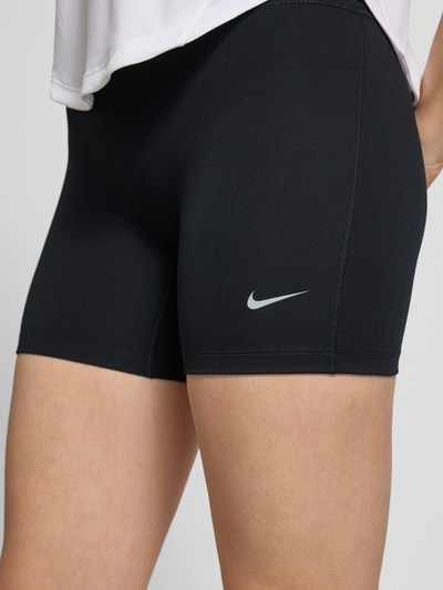 Frauenmodel trägt Radlerhose mit Logo und elastischem Bund von NIKE TRAINING, Material-Mix mit Stretch-Anteil, körpernahe Passform, Logo, elastischer Bund, Bundweite bei Größe S 25 cm, Innenbeinlänge bei Größe S 15 cm, schlichte schwarze Optik, weiche und glatte Textur. Nahaufnahme Oberschenkel.
