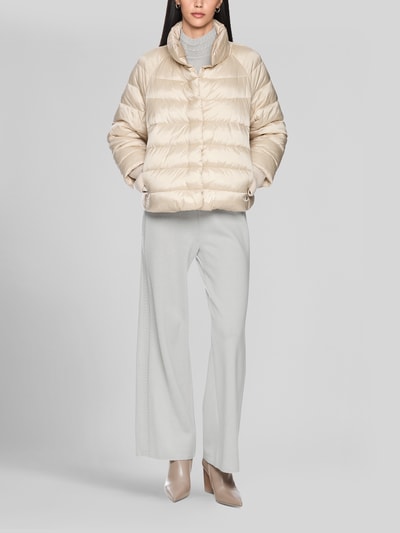 Frauenmodel trägt Steppjacke mit Stehkragen und Label-Detail von Marc Cain in Beige, strukturierte Oberfläche, Eingrifftaschen, Ganzkörperansicht von vorne. Rückenlänge 56 cm, Schulterbreite 41 cm, Brustweite 55 cm, Ärmellänge 73 cm, Regular Fit.