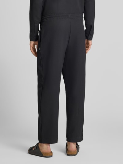 Männermodel trägt schwarze Hose mit elastischem Bund in Plissee-Optik von REVIEW, Material-Mix mit Stretch-Anteil, Regular-Fit, Ganzkörperansicht Rückansicht.