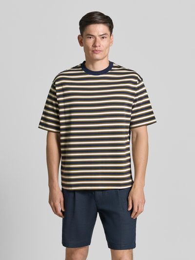 Mężczyzna-model ma na sobie męski t-shirt Relaxed Fit T-Shirt aus reiner Baumwolle Modell 'ASPEN 2' od SELECTED HOMME, paski w odcieniach granatu, kremu, żółci i brązu, gładka faktura, Ganzkörperansicht von vorne.