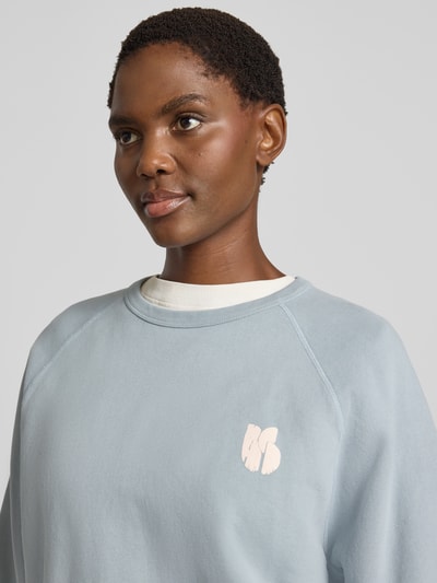 Vrouwenmodel draagt Relaxed Fit sweatshirt uit puur katoen met statementprint van ba&sh, lichtblauw, raglanmouwen, ribboorden, detailopname bovenlichaam.