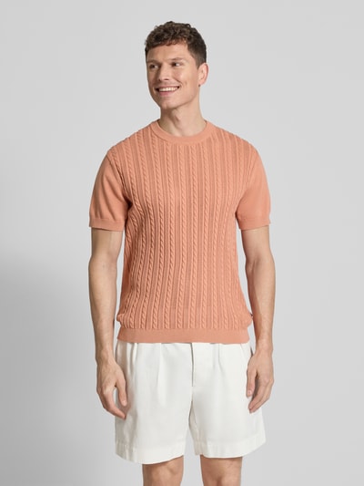 Männermodel trägt T-Shirt mit Zopfmuster von Lindbergh in Strick-Optik, reine Baumwolle, gerader Schnitt, lachsfarben, Ganzkörperansicht von vorne.