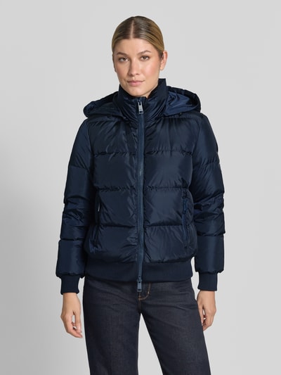 Frauenmodel trägt Steppjacke mit Daunen-Feder-Füllung von Armani Exchange in Dunkelblau, Kapuze, Zweiwege-Reißverschluss, Ganzkörperansicht von vorne. Elastischer Material-Mix, Regular Fit, Reißverschlusstaschen, Stehkragen, Rückenlänge 60 cm, Schulterbreite 41 cm, Brustweite 50 cm, Ärmellänge 62 cm.