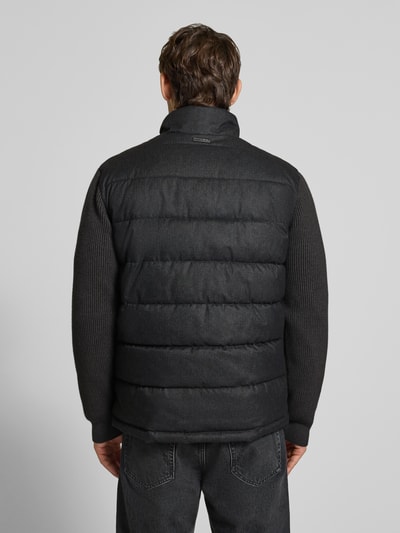 Männermodel trägt Steppjacke mit Stehkragen und Zweiwege-Reißverschluss von Christian Berg Men in Dunkelgrau, Ganzkörperansicht Rückansicht. Rückenlänge 70 cm, Schulterbreite 51 cm, Brustweite 60 cm, Ärmellänge 69 cm, glatte Stepptextur mit gestrickten Ärmeln.