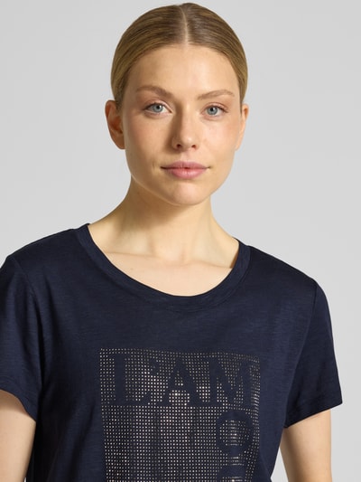 Frauenmodel trägt T-Shirt mit Ziersteinbesatz und Rundhalsausschnitt von monari aus Baumwoll-Micromodal-Mix in Regular-Fit, Nahaufnahme Oberkörper. Rückenlänge bei Größe 36: 58 cm.