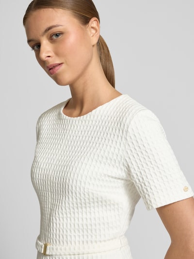 Kobiece model nosi Knielangens Kleid aus Baumwoll-Mix mit Strukturmuster od Marc Cain, mieszanka bawełny, okrągły dekolt, krótki rękaw, fakturowany wzór, detal z logo, widok z przodu, zbliżenie górnej części.