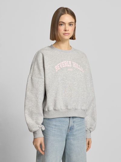 Frauenmodel trägt Sweatshirt mit Label-Print und Rundhalsausschnitt von Review aus Baumwoll-Mix im Relaxed-Fit, hellgrau, Ganzkörperansicht von vorne.