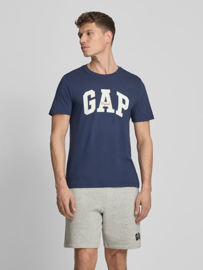 Männermodel trägt T-Shirt mit Logo und Rundhalsausschnitt von GAP in Blau, Reine Baumwolle, Regular-Fit, Rückenlänge 69 cm, Ganzkörperansicht von vorne.
