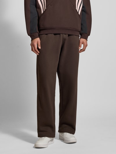 Männermodel trägt Straight Fit Sweatpants mit Logo-Stitching van adidas Originals, bruine katoen, elastische taille, Ganzkörperansicht von vorne.