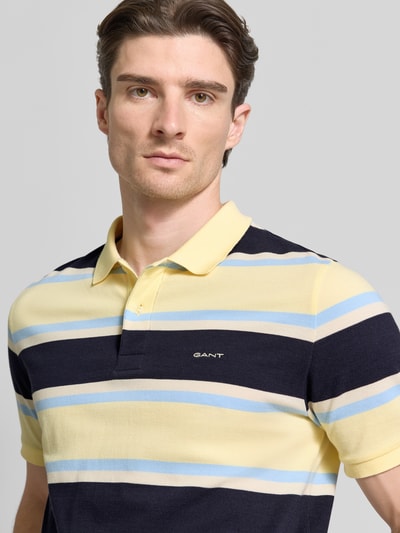 Männermodel trägt Slim Fit Poloshirt mit Logo-Stitching von Gant in Streifenoptik, reine Bio-Baumwolle, Nahaufnahme Oberkörper.