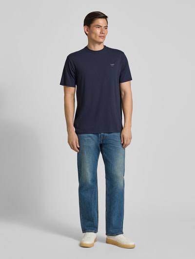 Männermodel trägt T-Shirt mit Logo und Rundhalsausschnitt von Guess in Dunkelblau, Baumwoll-Mix Modal, Relaxed Fit, Ganzkörperansicht von vorne.
