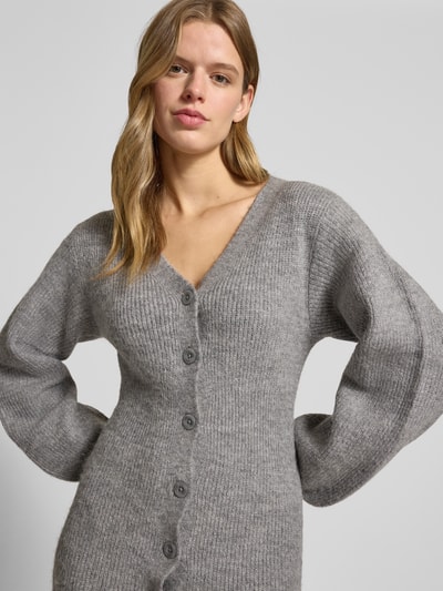 Kobiece modelka nosi Strickkleid mit V-Ausschnitt und Knopfleiste od Gina Tricot, mieszanka materiałów z domieszką wełny z alpaki, prosty krój, długa sukienka, dekolt w serek, listwa guzikowa, długość tyłu 138 cm, szerokość klatki piersiowej 40 cm, długość rękawów 66 cm, szary melanż, miękka faktura, proste linie, nahaufnahme górnej części ciała.