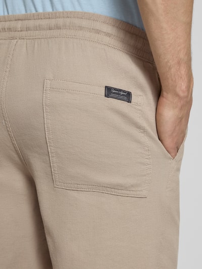 Męski model nosi Shorts mit Strukturmuster Modell 'JAIDEN' von Jack & Jones, bawełna, krój regular fit, elastyczny pas, teksturowana tkanina, beżowy kolor, szerokość w rozmiarze M: 43 cm, długość nogawki od wewnątrz: 23 cm, ujęcie detailaufnahme tylnej kieszeni