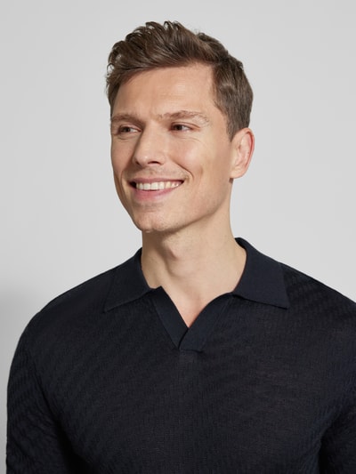 Männermodel trägt Slim Fit Poloshirt mit Lyocell-Anteil von Emporio Armani, Strick-Optik, dunkle Farbe, Nahaufnahme Oberkörper.