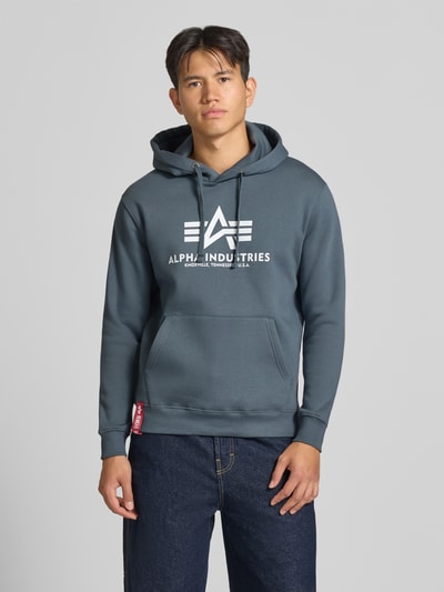Männermodel trägt Regular Fit Hoodie aus Baumwoll-Mix mit Logo-Print von Alpha Industries in Blau, elastische Abschlüsse, Nahaufnahme Oberkörper. Herren Hoodie, Kapuze mit Tunnelzug, Label am Saum, Rückenlänge 70 cm, Ärmellänge 64 cm.