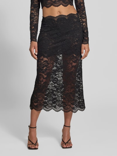 Vrouwenmodel draagt Midirok uit kant van Rabanne in zwart, rechte pasvorm, semi-transparant, geschulpte zoom, bloemenpatroon, elastische materiaalmix, tailleband, totale lengte maat 38: 85 cm, bandwijdte maat 38: 38 cm, detailopname onderlichaam.