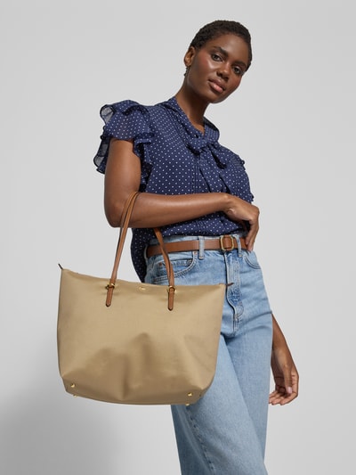 Kobiece modelka nosi Tote Bag z aplikacją z metką model 'KEATON' od Lauren Ralph Lauren, beżowa faktura, uchwyty, główna przegroda z zamkiem błyskawicznym, wymiary 37x28x13 cm, długość paska 54 cm, widok całej sylwetki z przodu.
