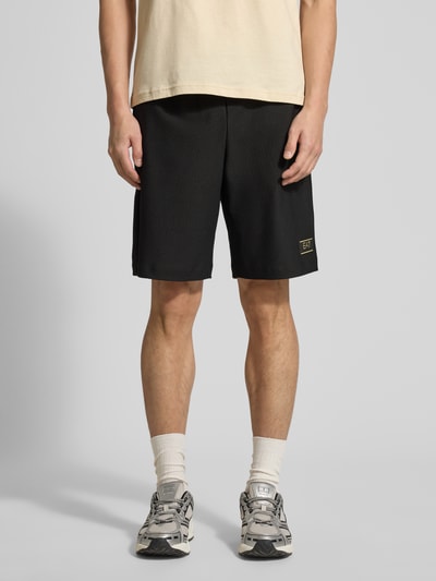 Männermodel trägt Regular Fit Shorts mit Strukturmuster von EA7 Emporio Armani in Schwarz, elastischer Bund, Ganzkörperansicht von vorne.