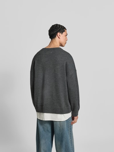 Männermodel trägt Oversized Pullover aus Woll-Mix von MM6 Maison Margiela in Dunkelgrau, Strick-Optik, Logo-Stitching, Rückenlänge 80 cm, Ganzkörperansicht Rückansicht.