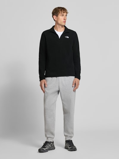Męski model nosi Fleecepullover mit Troyer-Kragen Modell 'GLACIER' od The North Face, prosty krój, wyhaftowane logo, widok całej sylwetki z przodu. Długość tyłu w rozmiarze M: 70 cm, długość rękawów w rozmiarze M: 73 cm.