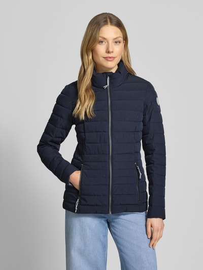 Modelka nosi kurtkę pikowaną z zamkiem błyskawicznym i kieszeniami zapinanymi na zamek błyskawiczny, model 'GS 111' od G.I.G.A. DX, krój slim fit, stójka, długość tyłu w rozmiarze 36: 67 cm, szerokość ramion w rozmiarze 36: 38 cm, szerokość klatki piersiowej w rozmiarze 36: 49 cm, długość rękawów w rozmiarze 36: 65 cm, granatowa, gładka struktura, prostokątne pikowanie, całkowity widok z przodu