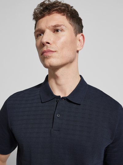 Männermodel trägt Regular Fit Poloshirt aus reiner Baumwolle von Marc O'Polo in Dunkelblau mit Gitterkaro Struktur, Nahaufnahme Oberkörper.