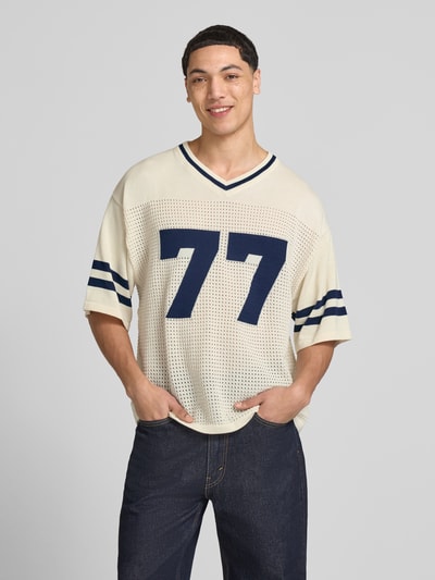 Männermodel trägt Strick-Trikot mit Jacquard Muster von REVIEW, prosty krój, dekolt w serek, rękaw o dł. 1/2, perforowanie, kolor ecru i granatowy, długość tyłu w rozmiarze M: 69 cm. Ganzkörperansicht von vorne.