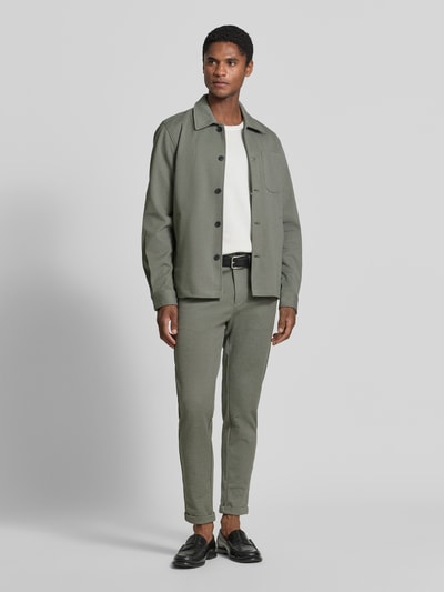 Männermodel trägt Slim Fit Hemdjacke mit Viskose-Anteil von Lindbergh in Olivgrün mit Umlegekragen, Ganzkörperansicht von vorne. Rückenlänge bei Größe M: 70 cm, elastischer Material-Mix, aufgesetzte Brusttasche, Eingrifftaschen, durchgehende Knopfleiste.