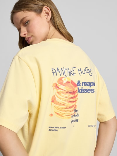 Frauenmodel trägt Oversized Damen T-Shirt aus Reine Baumwolle, Modell 'Pancake' von OH APRIL in hellgelb mit buntem Pancake-Print auf dem Rücken, Rundhalsausschnitt, glatte Textur, Rückenlänge bei Größe S: 69 cm, Ganzkörperansicht Rückansicht.
