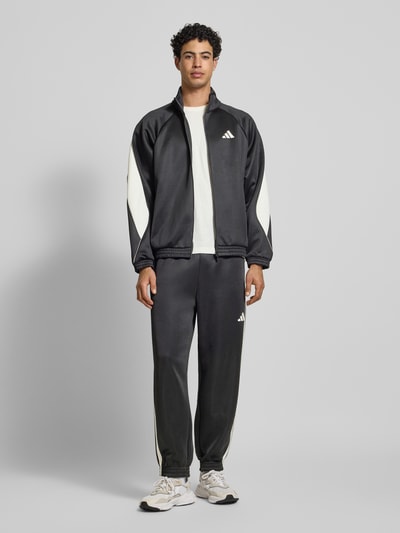 Männermodel trägt Sweatpants mit elastischem Bund von adidas Sportswear im schwarzen Material-Mix, Label-Print, Eingrifftaschen, Ganzkörperansicht von vorne.