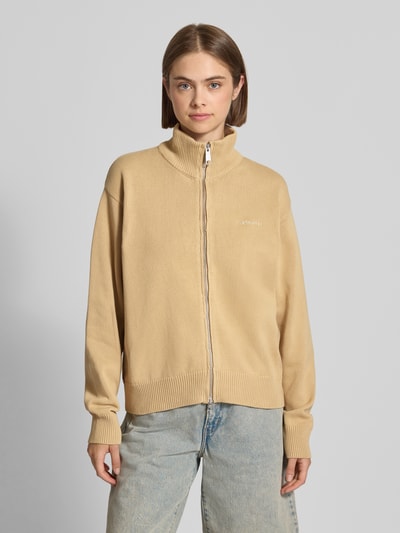 Frauenmodel trägt Cardigan mit Label-Stitching Modell 'Kori' von Carhartt Work In Progress in Beige, Stehkragen, Zweiwege-Reißverschluss, reine Baumwolle, Relaxed Fit, strukturierte Oberfläche, Jeans, Ganzkörperansicht von vorne.