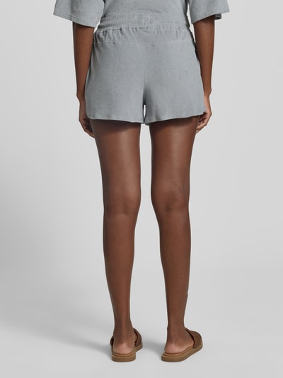 Frauenmodel trägt Straight Fit Shorts mit Tunnelzug Modell 'Saha' von Drykorn, graues Strukturmuster, elastischer Bund, Ganzkörperansicht Rückansicht.