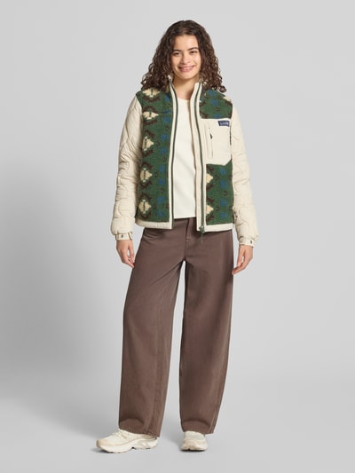 Frauenmodel trägt Fleecejacke mit Steppnähten und Label-Detail von Superdry in Creme und Grün, gerade Passform, Stehkragen, Reißverschluss, Brusttasche, weiche Textur, kombiniert mit brauner Hose und hellen Sneakers, Ganzkörperansicht von vorne. Rückenlänge 58 cm, Schulterbreite 39 cm, Brustweite 52 cm, Ärmellänge 65 cm.