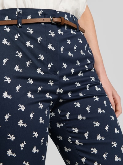 Vrouwenmodel draagt Hose im Allover-Look met riem van Christian Berg Woman, donkerblauw met witte bloemen, mix van katoen en viscose, slim fit, verkorte pasvorm, detailopname taille en dijen.