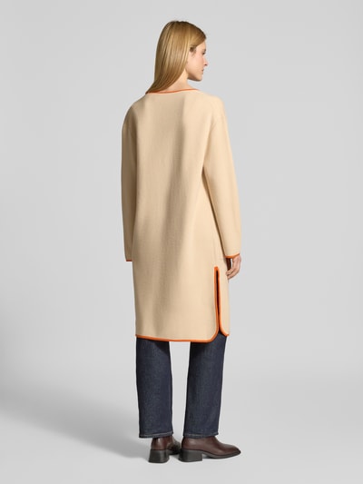 Frauenmodel trägt Strickmantel aus Baumwoll-Kaschmir-Mix mit aufgesetzten Taschen von HERZENS, beige mit orangem Saum, Relaxed-Fit, Rückansicht, Rückenlänge 99 cm, Ärmellänge 57 cm, offene Passform. Ganzkörperansicht Rückansicht.