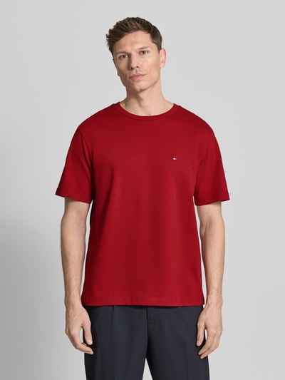 Männermodel trägt Relaxed Fit T-Shirt aus reiner Baumwolle von Tommy Hilfiger in Rot, unifarben, Rundhals, Logo-Stitching, Ganzkörperansicht von vorne.