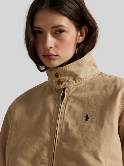 Vrouwenmodel draagt Regular Fit Blouson uit pure katoen van Polo Ralph Lauren in effen beige met logo-detail, elastische boorden, tweewegrits, zijflapzakken, opstaande kraag, lange mouw. Close-up bovenlichaam.