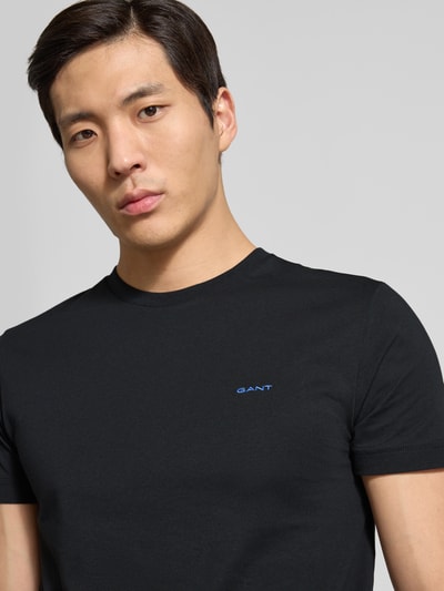 Männermodel trägt t-shirt met labeldetail van Gant in zwart, puur katoen, recht model, ronde hals, ruglengte maat M 70 cm, Nahaufnahme bovenlichaam.