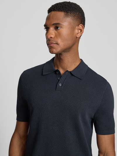Männermodel trägt Slim Fit Poloshirt Modell 'Triton' von Drykorn in Dunkelblau mit Strukturmuster aus Reine Baumwolle, Nahaufnahme Oberkörper.