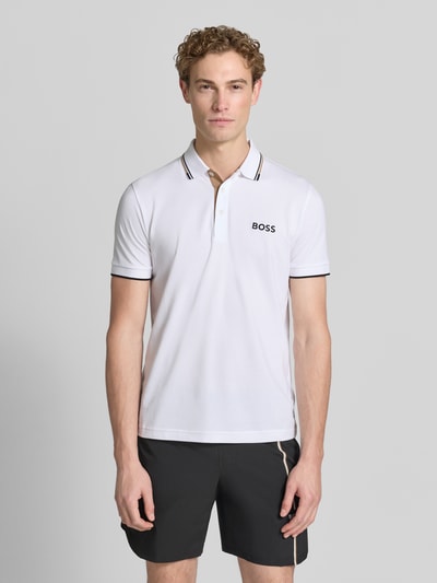 Mężczyzna nosi koszulkę polo Regular Fit model 'PADDY PRO' z mieszanki bawełny od BOSS Green, biały kolor, czarne akcenty, gładka tekstura, całkowity widok z przodu.