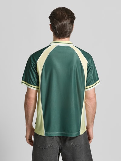 Männermodel trägt Poloshirt mit Label-Print Modell 'Taka' von WOODBIRD, lockere Passform, Polokragen, Kurzärmelig, Ganzkörperansicht Rückansicht.