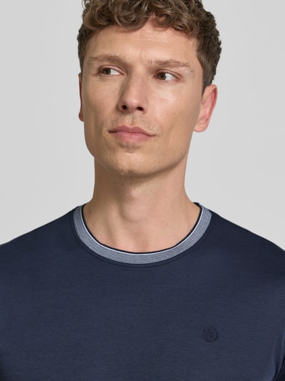 Mężczyzna nosi T-Shirt mit Rundhalsausschnitt von bugatti, mieszanka bawełny, krój regular fit, detal z logo, okrągły dekolt, zbliżenie na górną część ciała