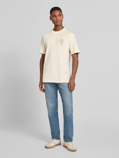 Męski model nosi T-Shirt mit rückseitigem Motiv-Print Modell 'Ben Faience' von Les Deux, jasny beż, czysta bawełna, krój regular fit, statement-print, widok całej sylwetki z przodu.
