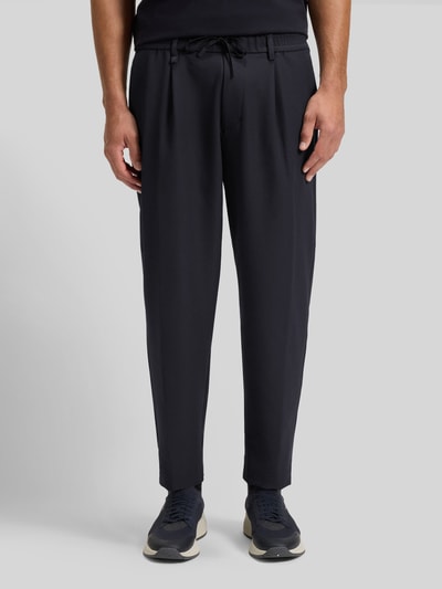 Männermodel trägt Tapered Bundfaltenhose mit halbelastischer Bund Modell 'CONVERT-PLEAT' von BOSS Green, unifarben, 4-weg stretch, met biesvouwen, tunnelkoord en riemlussen, zijzakken, Ganzkörperansicht von vorne.