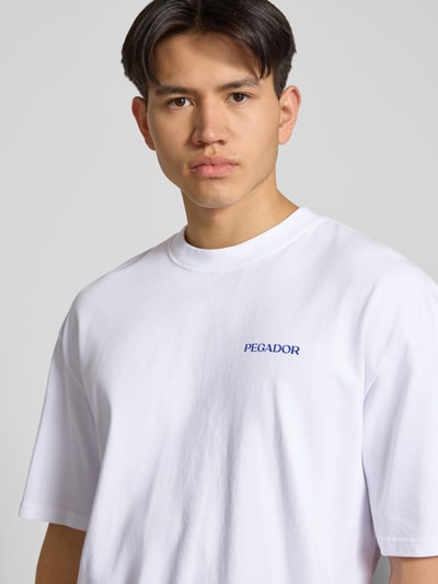 Männermodel trägt Oversized T-Shirt mit Rundhalsausschnitt Modell 'Frombork' von Pegador aus reiner Baumwolle mit Logo-Detail, Nahaufnahme Oberkörper.